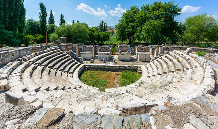 The semicircular marble seating of the Bouleuterion, the council house, at Aphrodisias, framed by trees.