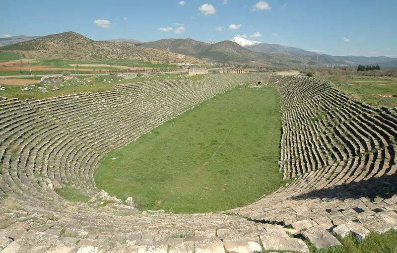The vast elongated stadium of Aphrodisias, its stone seating curving around a green field beneath the mountains of Caria.